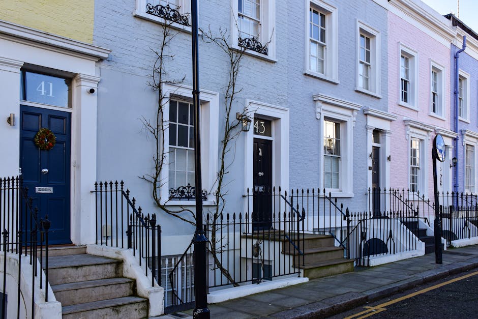 A view of a narrow city street in Soho, W1D, with red brick and pastel-colored residential buildings on either side. The street is paved with dark cobblestones and lined with red bollards. Decorative orange lanterns hang across the street, adding a festive touch. On the left, a modern glass building reflects the surrounding architecture. The scene is illuminated by natural daylight, creating a bright and clean atmosphere. Soho Carpet Cleaning's logo and branding are not visible in this image, as it depicts an outdoor urban setting rather than a clean interior surface. This image is suitable for illustrating urban environments or the need for professional cleaning services in commercial or residential settings, consistent with the page about end of tenancy cleaning for properties on Dean Street W1D.