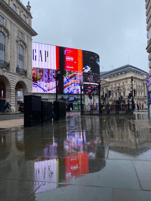Nighttime scene of Piccadilly Circus in Soho, featuring illuminated advertising billboards, including a large digital display with colorful visuals, surrounded by historic architecture with ornate fac