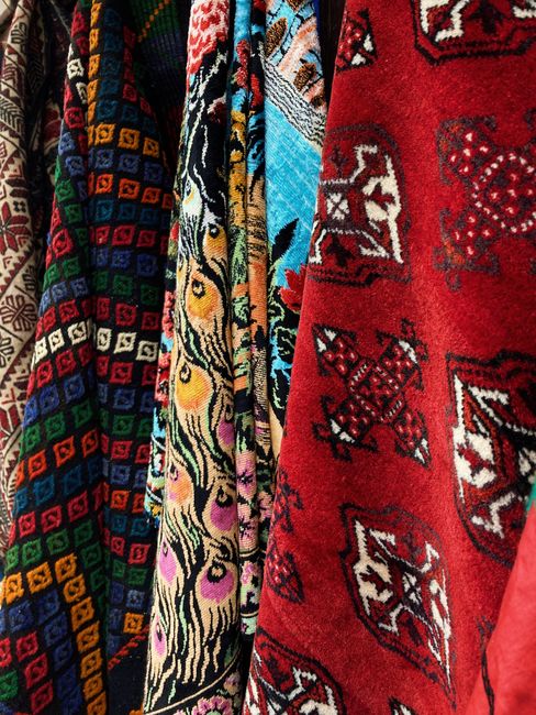 A close-up image of several hanging rugs with intricate patterns and vibrant colors, including red, black, blue, yellow, and purple. The rugs feature geometric and floral designs typical of traditional textile art. They are suspended in an indoor setting with soft, neutral lighting that highlights the detailed craftsmanship. The surfaces appear clean and well-maintained, reflecting professional cleaning standards. This image exemplifies surface cleaning and maintenance of decorative textile flooring, relevant to Soho Carpet Cleaning's expertise in deep cleaning and sanitisation of domestic and commercial rugs. The arrangement emphasizes the quality and appearance of the rugs, which are part of the cleaning services offered in Soho Square, W1.
